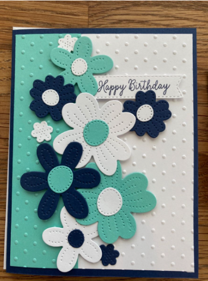 50+ Easy DIY Crafts to Sell and Make Extra Money Easy DIY crafts to sell: A handmade birthday greeting card featuring an embossed polka-dot background in white and teal, decorated with layered paper cutout flowers in navy blue, white, and teal, and a small banner stamped with the text "Happy Birthday".