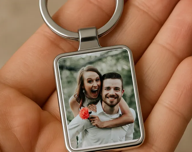 50+ Easy DIY Crafts to Sell and Make Extra Money Easy DIY crafts to sell: A rectangular metal photo keychain held in the palm of a hand, featuring a custom printed picture of a smiling couple embracing outdoors with a small red flower accent.