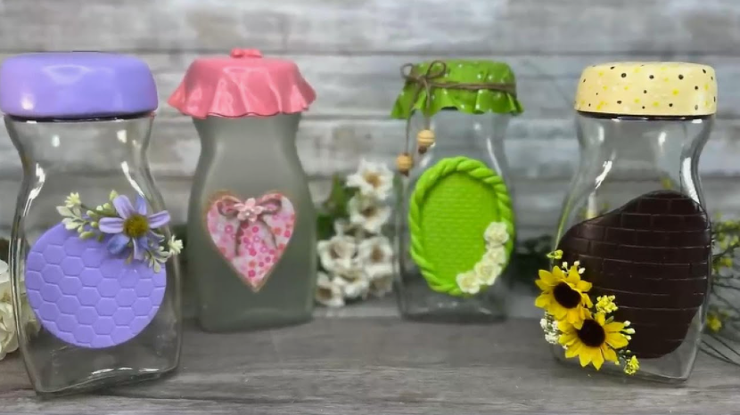 50+ Easy DIY Crafts to Sell and Make Extra Money Easy DIY crafts to sell: Four decorative glass jars with colorful lids, featuring customized clay and floral embellishments including a purple honeycomb design, a pink heart applique, a green textured frame, and a dark brown patch accented with yellow sunflowers.
