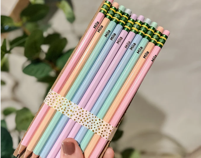 50+ Easy DIY Crafts to Sell and Make Extra Money Easy DIY crafts to sell: A bundle of pastel-colored personalized pencils featuring the name "Mila" printed along the barrel, tied together with a gold polka-dot decorative ribbon.