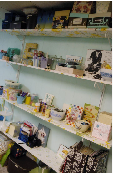 50+ Easy DIY Crafts to Sell and Make Extra Money Easy DIY crafts to sell: A well-organized craft room shelving unit featuring multiple tiers filled with decorative storage boxes, jars, art supplies, framed prints, and craft materials.