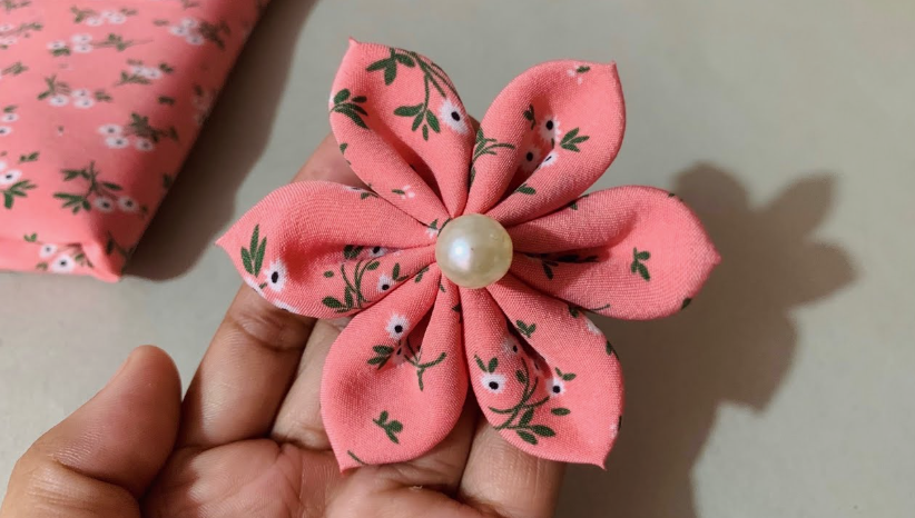 50+ Easy DIY Crafts to Sell and Make Extra Money Easy DIY crafts to sell: A handmade fabric flower held in a hand, featuring folded pink floral-print petals and a central white faux pearl bead.