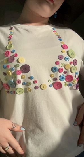 50+ Easy DIY Crafts to Sell and Make Extra Money Easy DIY crafts to sell: A white t-shirt embellished with colorful sewn-on buttons arranged in a whimsical corset or bra-top pattern across the front.