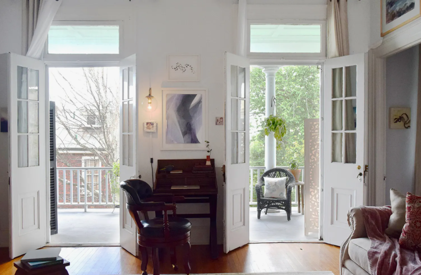 Small Living Room Decor Ideas on a Budget: 25 Stylish Ways to Make It Look Expensive Bright living room featuring small living room decor ideas on a budget with double French doors opening to a balcony, a dark wood secretary desk and chair, framed wall art, and a portion of a cozy sofa with pink and red pillows.
