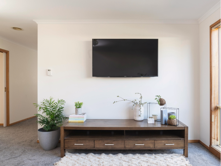Small Living Room Decor Ideas on a Budget: 25 Stylish Ways to Make It Look Expensive Modern living room featuring small living room decor ideas on a budget with a wooden TV media console with drawers, a wall-mounted flat-screen television, a potted palm plant, and decorative table accents.