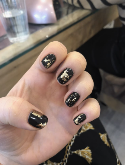 Short nail designs featuring glossy black polish accented with shimmering gold foil flakes.
