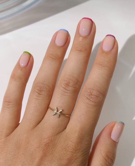 Short nail designs featuring colorful pastel French tips in different shades like green, blue, and purple on a neutral glossy base.