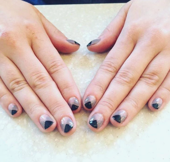 Short nail designs featuring geometric black triangle cutouts at the cuticle on a neutral, glossy base.
