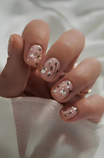 Short nail designs featuring delicate hand-painted white floral botanical art with dark stems on a neutral glossy base.