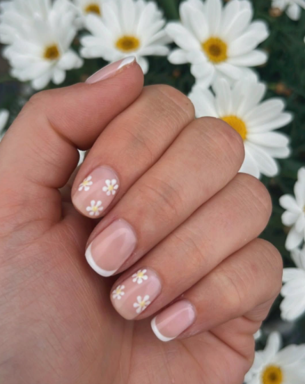 Short nail designs featuring alternating classic white French tips and cute hand-painted white daisy flowers with yellow centers on a neutral glossy base.