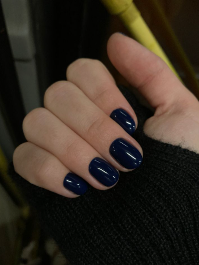 Short nail designs featuring glossy dark navy blue polish on neatly rounded short nails.