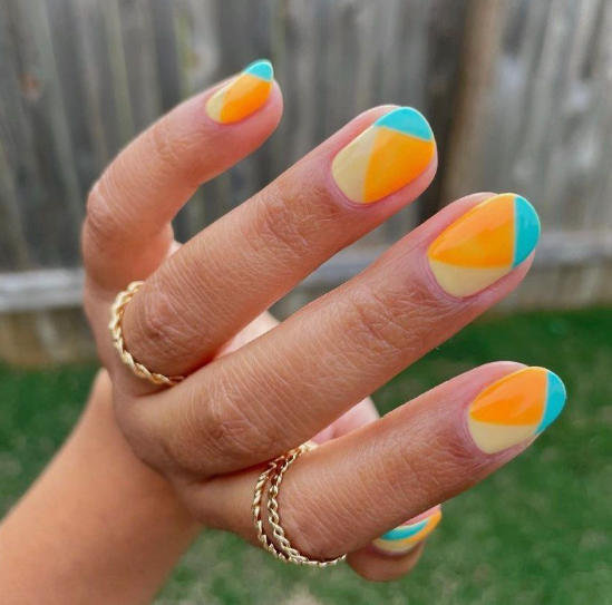 Short nail designs featuring vibrant color-blocked geometric segments in bright orange, turquoise, and soft cream on glossy rounded short nails.
