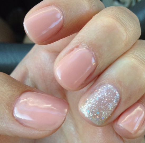 Short nail designs featuring glossy solid soft peach-pink polish paired with a sparkling reflective glitter accent nail on neat square nails.
