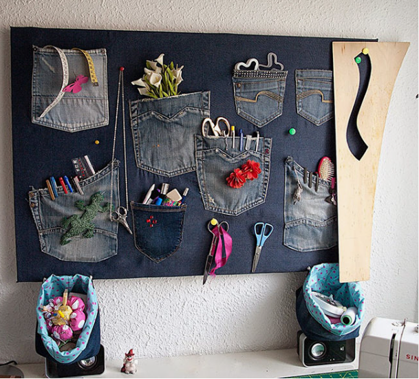 A wall organizer board made from recycled denim featuring multiple jean pockets used to hold craft supplies and tools for DIY crafts using things you have at home.