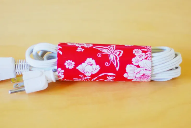 A coiled white electrical cord secured neatly with a red floral patterned paper band for DIY crafts using things you have at home.