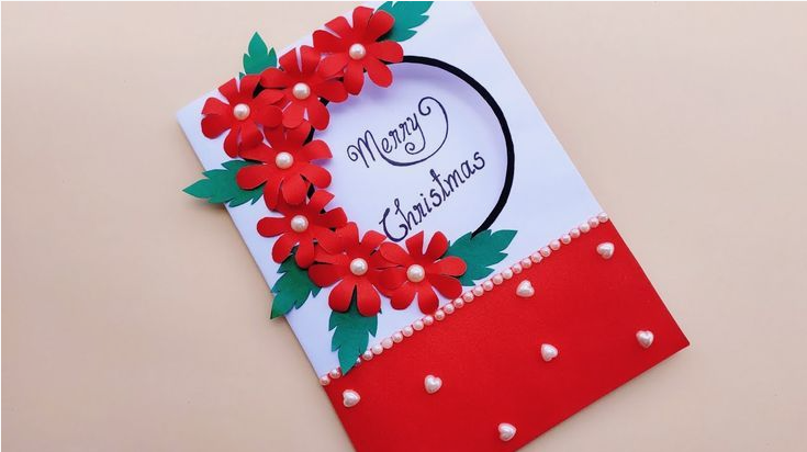 A handmade Merry Christmas greeting card decorated with paper red flowers, green leaves, and pearl beads for DIY crafts using things you have at home.