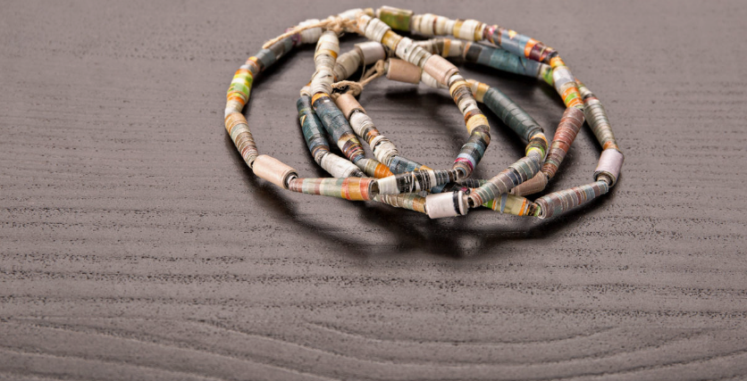 A necklace made of colorful rolled paper beads resting on a dark wooden surface, highlighting DIY crafts using things you have at home.