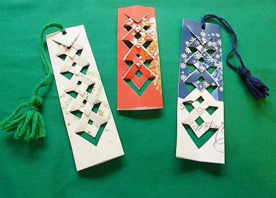 Three handmade bookmarks featuring intricate woven and cut-out paper patterns with matching yarn tassels for DIY crafts using things you have at home.