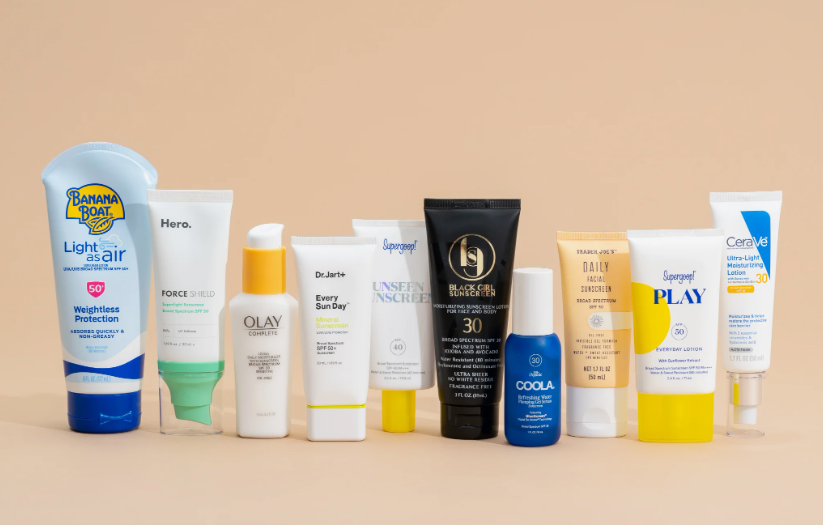 Line-up of top-rated beauty products worth buying featuring an assortment of facial sunscreens and lotions from brands like Banana Boat, Hero, Olay, Dr. Jart+, Supergoop, Black Girl Sunscreen, Coola, Trader Joe's, and CeraVe arranged against a neutral background.