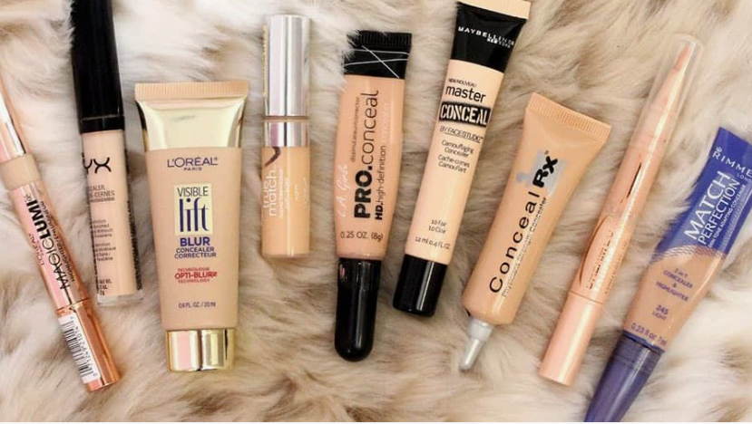 Flat lay of popular concealer tubes and correctors from brands like L'Oreal, NYX, Maybelline, and Rimmel, showcasing beauty products worth buying arranged on a furry background.