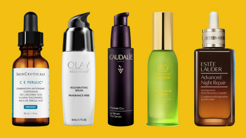 An assortment of luxury beauty products worth buying featuring high-end serums from brands like SkinCeuticals, Olay, Caudalie, Tata Harper, and Estée Lauder arranged against a vibrant yellow background.