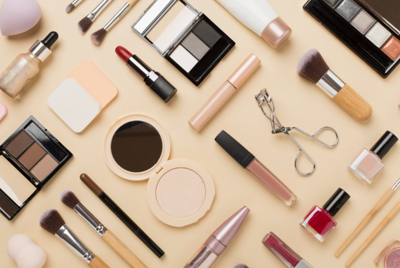 Flat lay of beauty products worth buying featuring an assortment of makeup items, eyeshadow palettes, lipsticks, brushes, and nail polish arranged on a neutral background.