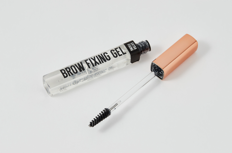 The Minimal Makeup Guide: How to Look Polished With Less Makeup An open tube of clear brow fixing gel with its spoolie applicator wand resting next to it on a clean white surface.