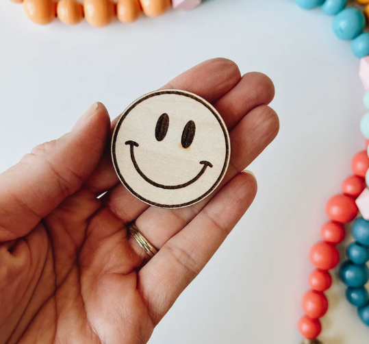A person holding a small round wooden disc with an engraved smiley face, showcasing fun air dry clay ideas and craft projects.