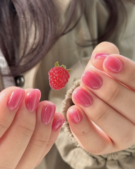 Glossy berry pink short nails holding a raspberry, showcasing low-maintenance nail designs.