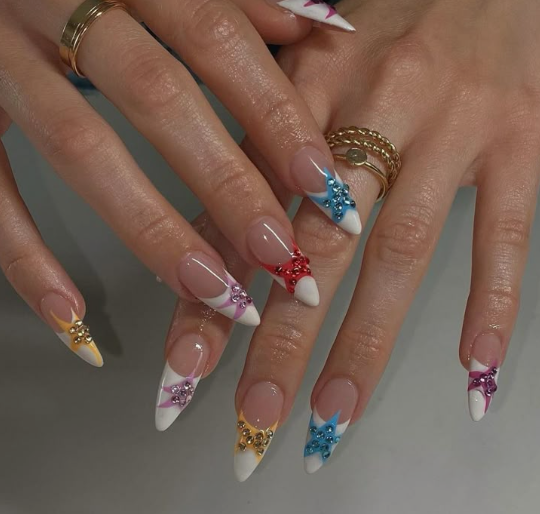 15 Stunning 3D Nail Designs to Try This Season Glamorous 3D nail designs featuring French tips adorned with sparkling gemstone starbursts in various colors.