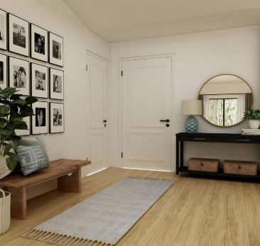 A bright, modern entryway featuring light wood floors, a gallery wall of black-and-white photos, a wooden bench with blue patterned pillows, and a black console table styled to look expensive on a budget.