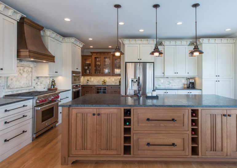 A spacious, modern kitchen featuring white and wooden cabinetry, a large central island with built-in wine storage and dark stone countertops, hanging pendant lights, and stainless steel appliances.