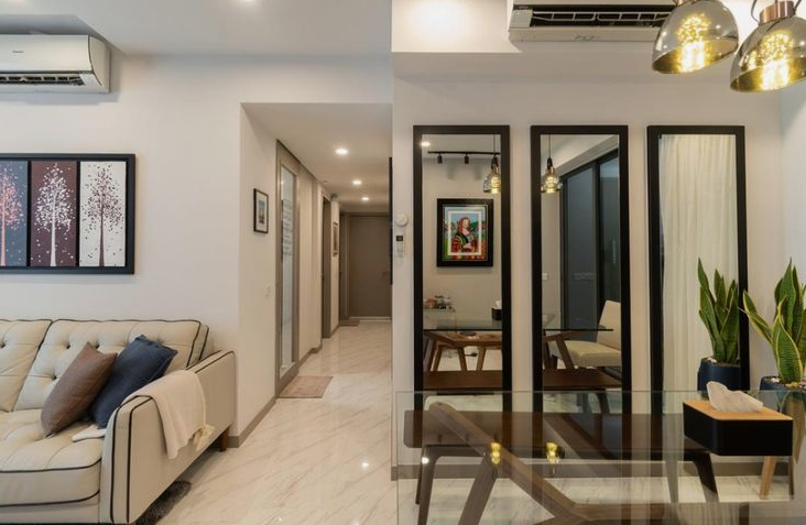 A contemporary living and dining area featuring a light tufted sofa, a glass-topped dining table, and three large floor-to-ceiling mirrors with sleek black frames, strategically positioned to reflect light and expand the space.