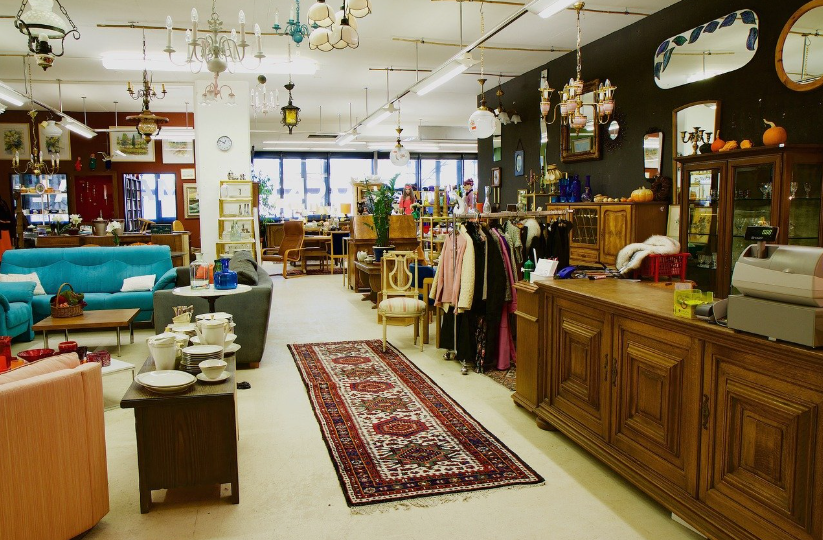 A thrift and antique store filled with secondhand vintage furniture, wooden cabinets, a Persian-style runner rug, and unique home decor items, showcasing ways to find budget-friendly, high-end pieces.