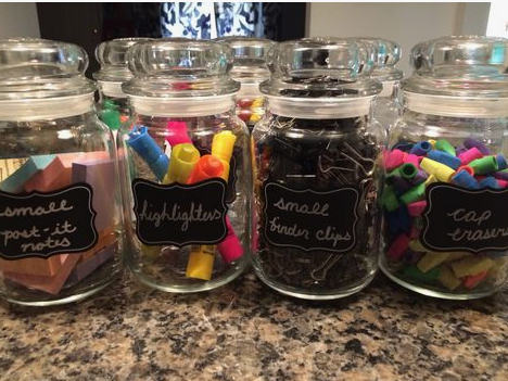 A glass canister labeled with a chalkboard sticker reading "small post-it notes" and filled with pastel sticky notes.