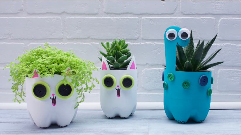 DIY plastic bottle planters shaped like cute animals, including two cat designs with button eyes and a blue dinosaur design with googly eyes and button spots, each holding potted greenery.