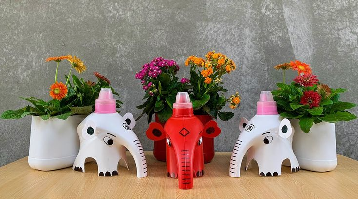 DIY planters crafted from plastic bottles shaped like elephants, featuring painted details and holding colorful potted flowers.
