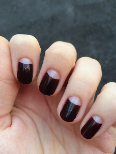 Short, neatly-rounded nails featuring a chic half-moon manicure with deep dark burgundy polish and bare, semi-circle cutouts at the base, serving as a stylish example of easy nail designs for short nails.