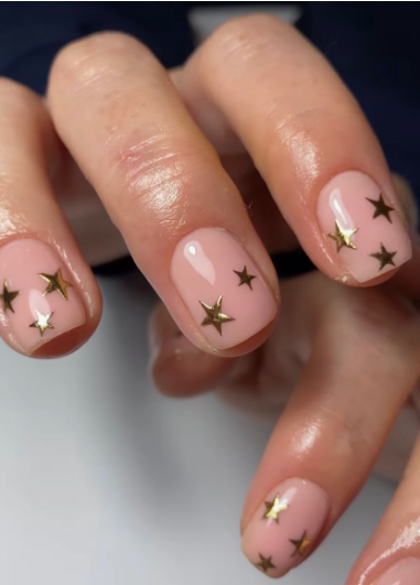 Short, rounded nails featuring a glossy translucent nude base decorated with scattered metallic gold star decals, serving as a charming and simple choice for easy nail designs for short nails.