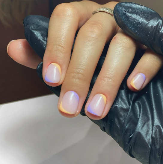 Short, square-cut nails featuring a soft nude base accented with delicate, pastel-toned yellow and purple diagonal tips, offering a fresh inspiration for easy nail designs for short nails.