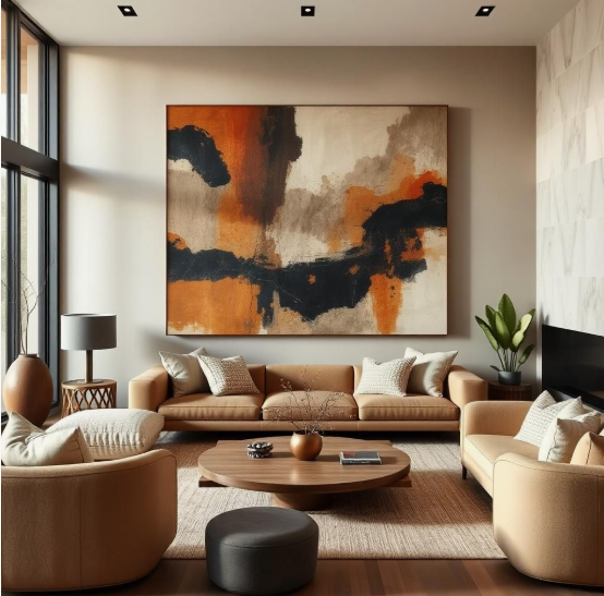 A contemporary living room featuring a warm beige sofa and matching armchairs arranged around a round wooden coffee table, a dark grey ottoman, and a large abstract painting with black, orange, and white tones hanging on the wall, offering modern inspiration for renter-friendly home decor ideas.