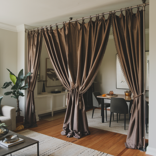A creative room divider featuring rich brown fabric curtains hung from a tension rod system, partially partitioning a living area and dining space while offering functional and stylish inspiration for renter-friendly home decor ideas.