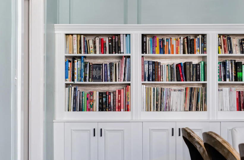 A built-in white bookshelf wall filled with neatly organized books and records, featuring lower cabinet storage and panel detailing, offering classic and functional inspiration for renter-friendly home decor ideas.