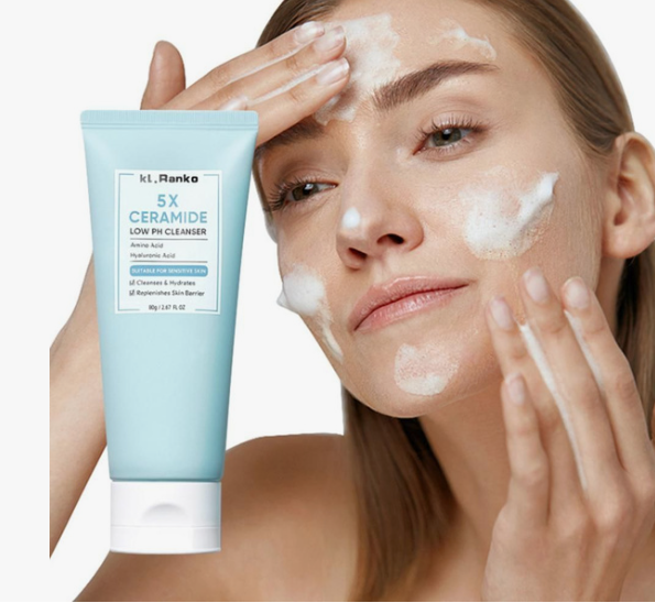A close-up of a woman cleansing her face with a foaming wash while holding a blue tube of Kiott Ranko 5X Ceramide Low pH Cleanser, offering an essential visual for a simple skincare routine for beginners.
