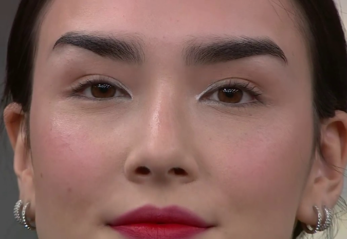 A close-up beauty portrait highlighting Spring 2026 makeup trends, featuring bold dark eyebrows, subtle light eyeshadow, radiant skin, and vibrant reddish-pink lips.
