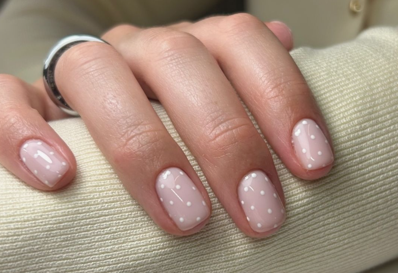Short, rounded nails featuring a glossy translucent pink base coat and delicate white polka dots, ideal for inspiration when looking for nail designs for short nail beds.