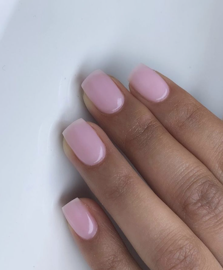 Short, squoval-shaped nails with a translucent light pink polish layer, serving as a stylish example of nail designs for short nail beds.