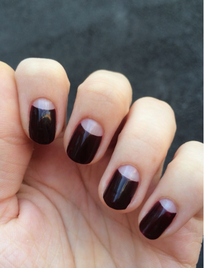 Short, rounded nails featuring a deep dark burgundy or black polish with contrasting nude half-moon cutouts at the base, serving as a bold option for nail designs for short nail beds.