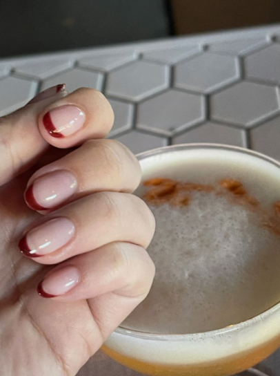 Short, rounded nails with a glossy nude base and thin, elegant deep burgundy tips, providing a sophisticated look for nail designs for short nail beds.