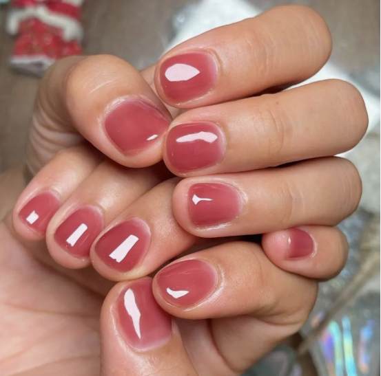 Short, rounded nails with a glossy translucent pinkish-mauve jelly finish, offering a sleek style for nail designs for short nail beds.